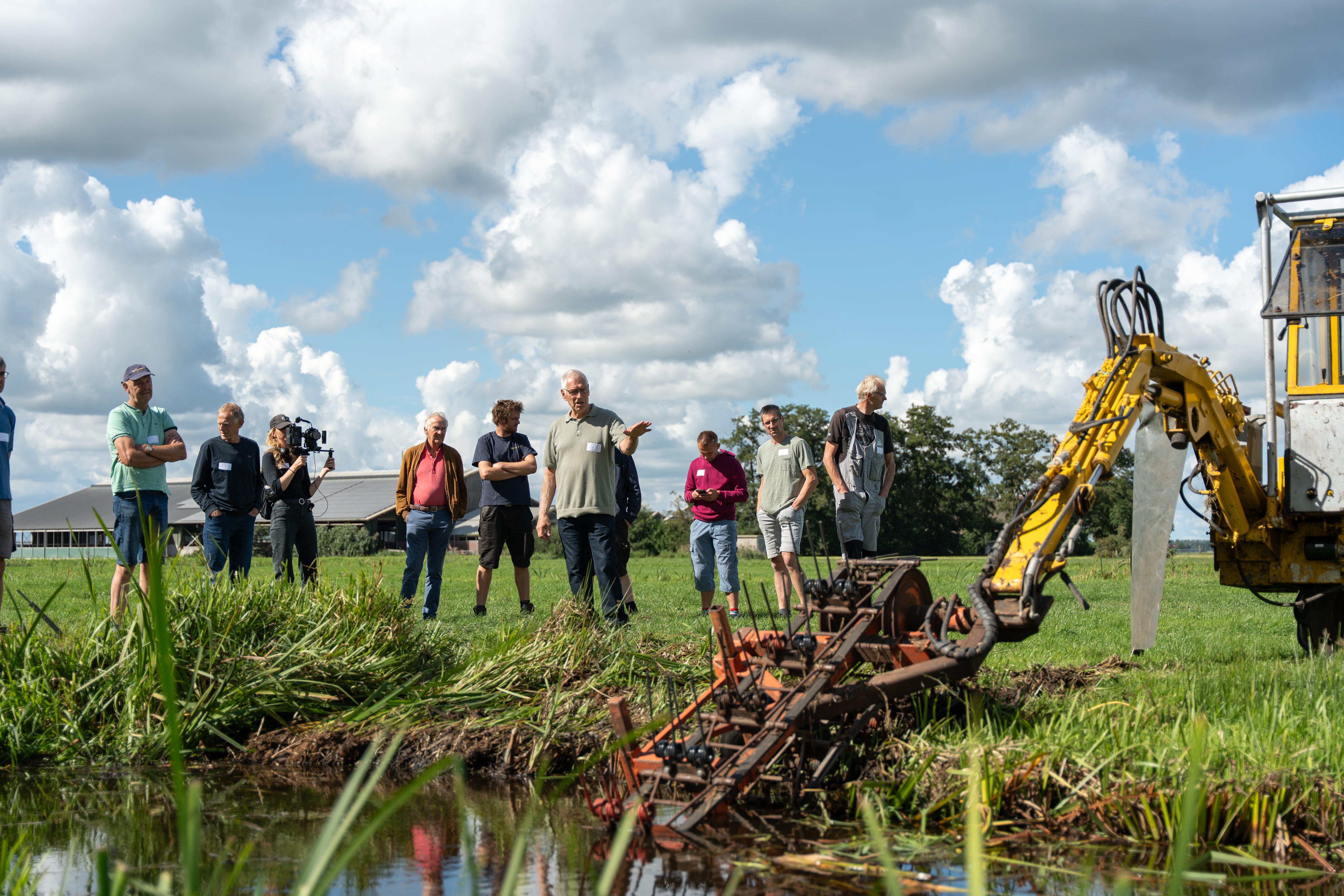Demonstratie van een slootschoon-machine met een boer die uitlegt en publiek wat luistert.